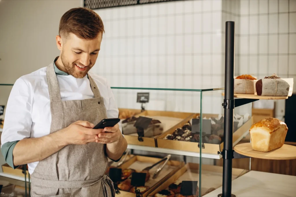 Smiling bakery owner checking his Google Business Profile on a smartphone behind the counter
